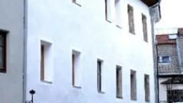 Historisches Gebäude mit weißer Fassade, mehreren Fenstern und charakteristischen Bogenöffnungen im Erdgeschoss.