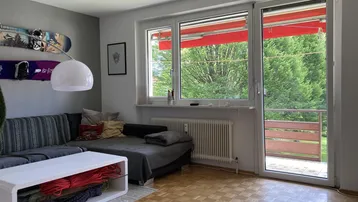 Helles Wohnzimmer mit gemütlichem Sofa, Parkettboden und Zugang zum Balkon mit grüner Aussicht.