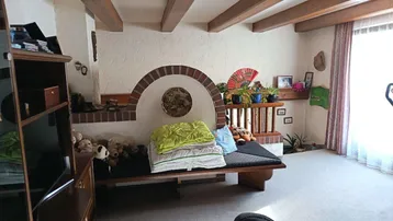 Helles Wohnzimmer mit Teppichboden, Holzbalken und einem gemauerten Kamin mit integrierter Sitzbank.