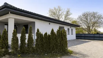 Modernes Einfamilienhaus mit weißer Fassade, Kiesauffahrt und grüner Hecke unter blauem Himmel.