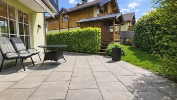 Sonnige Terrasse mit Steinplatten, Gartenmöbeln und Blick auf den gepflegten Gartenbereich.