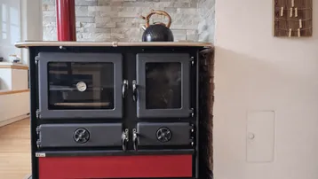 Traditioneller Holzofen mit rotem Sockel und Steinwand im Hintergrund.