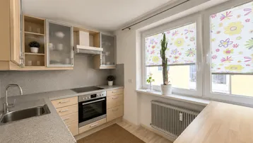 Funktionale Küche mit hellen Holzschränken, Einbaugeräten und einem Fenster mit bunten Rollos.