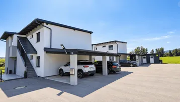 Moderne Wohngebäude mit Carports und gepflegter Außenanlage unter blauem Himmel.