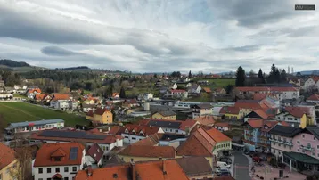Weitläufige Luftaufnahme einer ländlichen Siedlung mit vielen Häusern und grünen Hügeln im Hintergrund.
