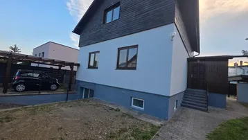 Einfamilienhaus mit weißer und dunkelgrauer Fassade, Carport und gepflastertem Zugang.