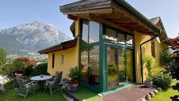 Charmantes Haus mit gelber Fassade, großer Glasfront, Garten und beeindruckendem Bergblick.