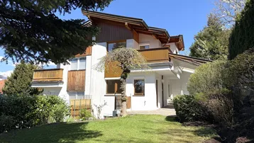 Großzügiger Gartenbereich vor einem charmanten Haus mit weißer Fassade und Holzelementen unter blauem Himmel.