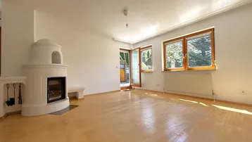 Helles Wohnzimmer mit traditionellem Kachelofen, Parkettboden und großen Fenstern mit Blick ins Grüne.
