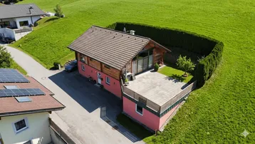 Drohnenaufnahme eines Einfamilienhauses mit roter Fassade, großem Garten und Photovoltaikanlage auf dem Nachbardach.