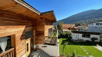 Holzverkleidetes Haus mit Außentreppe, Balkon und gepflegtem Gartenbereich in sonniger Berglage.
