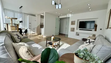 Helles, offenes Wohn- und Esszimmer mit modernem Sofa, Holzboden und integrierter Küchenzeile.