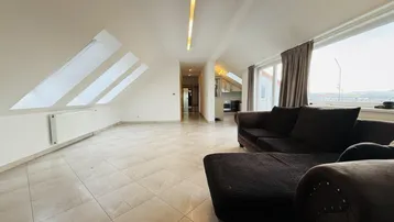 Geräumiges Wohnzimmer mit schrägen Wänden, Fliesenboden und Dachfenstern für Tageslicht.