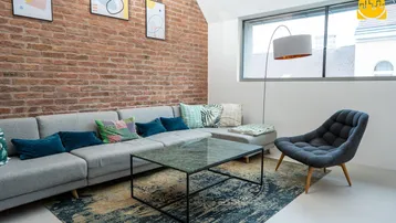 Modernes Wohnzimmer mit freiliegender Ziegelwand, großem Sofa und Blick nach draußen.