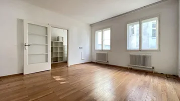Helles Wohnzimmer mit Holzboden und zwei großen Fenstern, die viel Tageslicht hereinlassen.