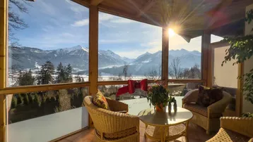 Heller Wintergarten mit Korbmöbeln und atemberaubendem Panoramablick auf die verschneiten Berge.