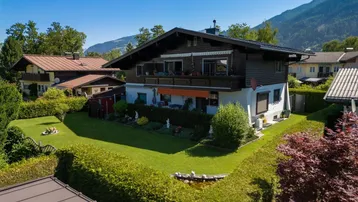 Luftaufnahme des Hauses mit gepflegtem Garten, Rasenfläche und Hecken, umgeben von Bergen.