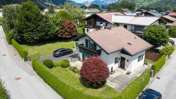 Vogelperspektive eines Einfamilienhauses mit gepflegtem Garten, Auffahrt und Bergblick.