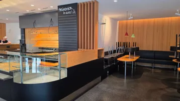 Moderner Innenbereich eines Cafés oder einer Bäckerei mit Theke, Holzwänden und Sitzgelegenheiten.