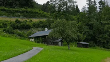 Ländliches Haus in grüner Umgebung mit Bäumen und einem Apfelbaum unter bewölktem Himmel.
