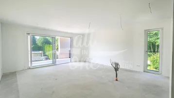 Heller, unfertiger Wohnraum mit Betonboden, großen Schiebetüren und französischem Balkon.