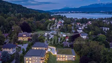 Abendliche Luftaufnahme moderner Wohngebäude mit Blick auf den See und die umliegende Berglandschaft.
