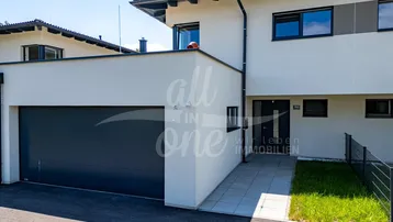 Moderne Doppelhaushälfte mit integrierter Garage und gepflegtem Eingangsbereich unter blauem Himmel.