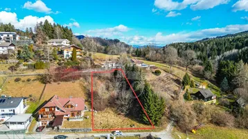 Luftaufnahme eines Baugrundstücks mit roter Markierung in ländlicher Umgebung und Bergblick.