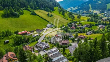 Panoramablick auf ein malerisches Dorf in einem grünen Tal, umgeben von bewaldeten Bergen.