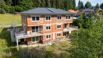 Neubau im Rohbauzustand mit mehreren Balkonen und Blick ins Grüne.