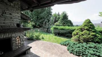 Überdachte Terrasse mit rustikalem Steinkamin und Blick auf den gepflegten Gartenbereich.
