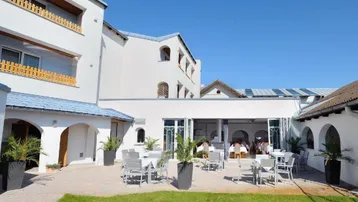 Große Außenterrasse mit Tischen und Stühlen, umgeben von einem gepflegten Rasen und dem Hotelgebäude.