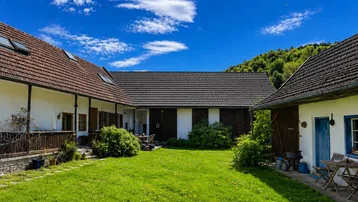 Idyllischer Innenhof mit grünem Rasen, umgeben von traditionellen Gebäuden und mit Blick auf bewaldete Hügel.