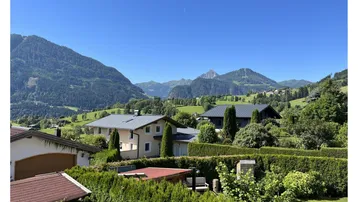 Panoramablick auf die umliegende Berglandschaft und grüne Hügel an einem sonnigen Tag.