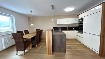 Moderne offene Küche mit Essbereich, Holzboden und Blick ins Grüne durch das Fenster.