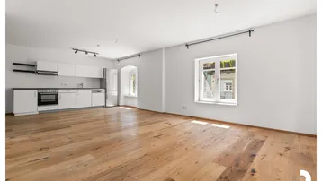 Heller offener Wohnbereich mit integrierter Küche, Holzboden und einem Fenster mit Blick nach draußen.