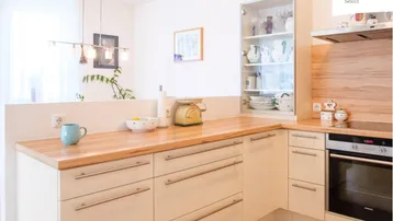 Moderne Küche mit hellen Holz-Arbeitsplatten, cremefarbenen Schränken und integrierten Geräten.