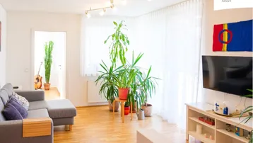 Helles Wohnzimmer mit Parkettboden, vielen Pflanzen und einem bequemen Sofa.
