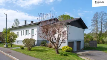 Ansicht des Hauses von vorne mit zwei Garagen und gepflegtem Vorgarten unter blauem Himmel.