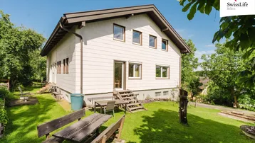 Großer Gartenbereich mit Rasenfläche, Bäumen und rustikalen Sitzgelegenheiten im Freien.