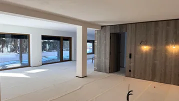 Geräumiger offener Wohnbereich im Rohbau mit großen Fensterfronten und Holzwandelementen.