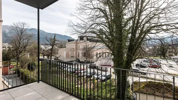 Balkon mit weitem Blick auf alte Bäume, historische Gebäude und die dahinterliegende Berglandschaft.