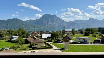 Spektakulärer Blick von einem Balkon auf einen See, Berge und ein malerisches Dorf.