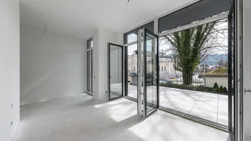 Helles, unmöbliertes Zimmer mit großen Falttüren, die zu einer geräumigen Terrasse führen.