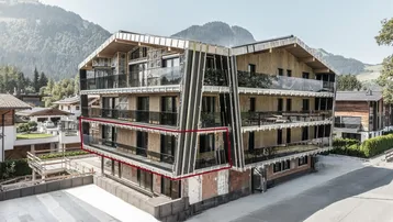 Modernes Apartmentgebäude in den Bergen mit Holzfassade und Glasbalkonen, teilweise noch im Bau.
