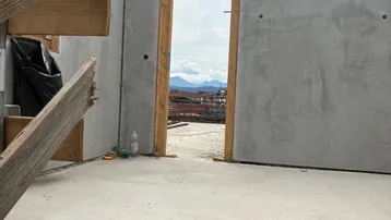 Rohbau mit Betonwänden und Türöffnung, die einen Blick auf die Berge freigibt.