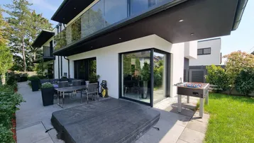 Große moderne Terrasse mit Outdoor-Sitzbereich, Whirlpool und Tischfußball, umgeben von viel Grün.
