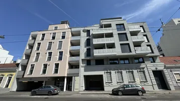 Modernes Mehrfamilienhaus mit Balkonen und großen Fenstern an einer Stadtstraße.