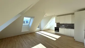 Heller Wohn- und Essbereich mit Dachschrägen, Holzboden und integrierter Küchenzeile.