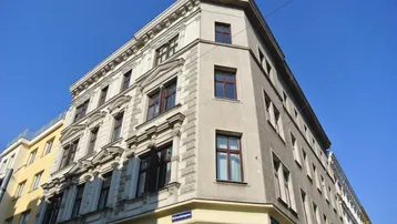 Historisches Eckgebäude mit klassischer Fassade und verzierten Fenstern unter blauem Himmel.